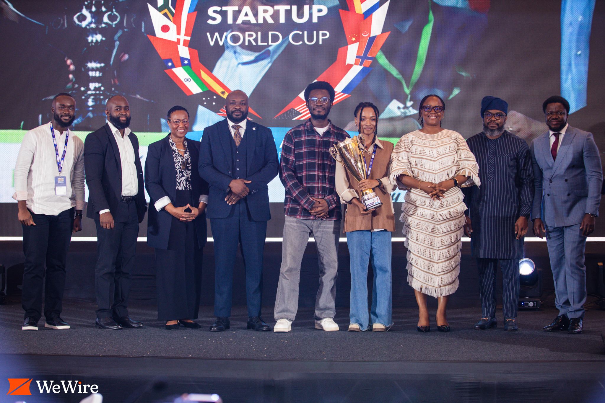 A group photograph on stage with the trophy and Startup World Cup backdrop.