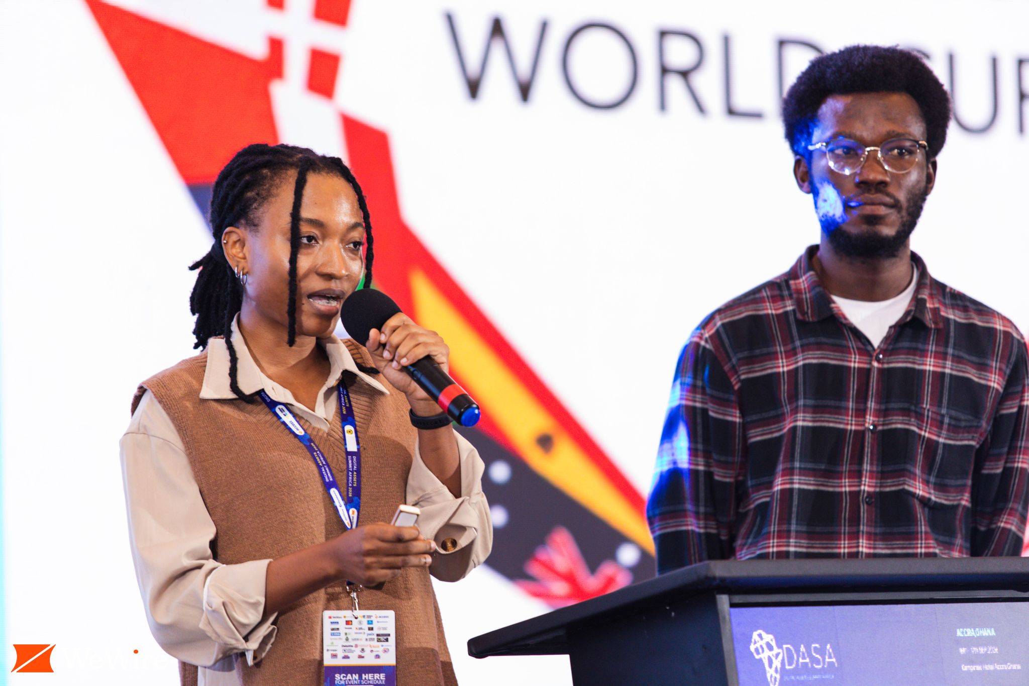 A presenter speaks into a microphone beside another presenter on stage.